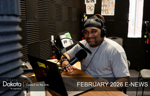 Smiling African American man sitting next to a computer and a microphone in a sound-proof podcasting room