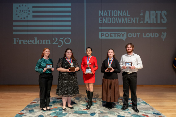 Five high schoolers stand on a stage holding awards in front of a National Endowment for the Arts Poetry Out Loud backdrop.