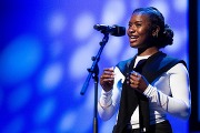 Jayda Dawn, a black female Indiana high schooler speaking poetry into a microphone on a stage with a blue background