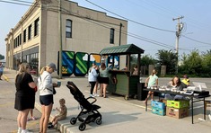 Community celebration of a public art mural; people are getting coffee and treats from food stands with the 58012 mural in the background