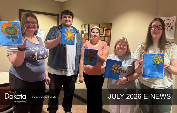 Five young adults with differing abilities, standing, smiling, and holding up their canvas artworks: flowers on blue backgrounds