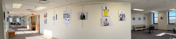 Art exhibit in long hallway taken in panoramic, white walls and plain floors with big windows throwing light on the walls