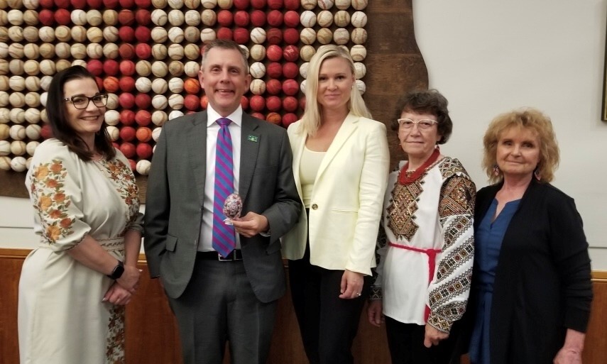 4 adults in Ukrainian clothing, standing with Governor Armstrong who is holding a pysanka egg he received for America 250