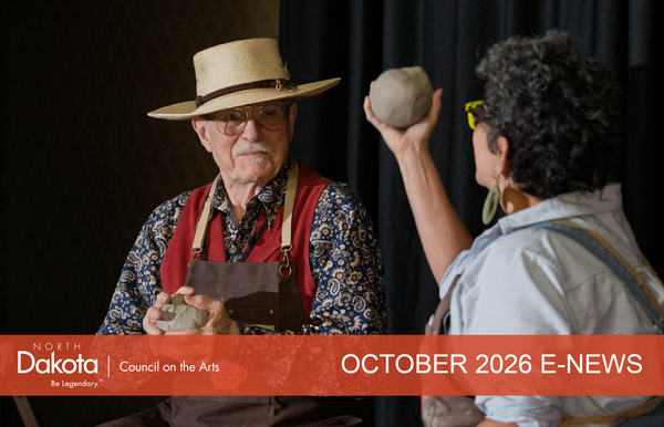 ND artists Walter Piehl (smiling) and Shelly Sayler (backside) sitting on a stage, holding a ball of clay in preparation for throwing on a wheel