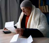 man in stocking cap and blanket paying bills