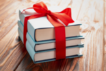 Stack of three books tied with a red ribbon with a bow on a wooden background