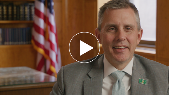 Governor Kelly Armstrong smiling at the camera with a play icon above his left shoulder