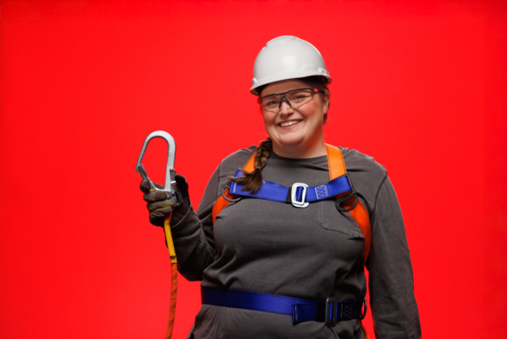 Photo of woman wearing a roofing harness, safety glasses, and hard hat smiling at camera
