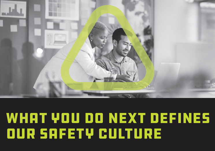 Black and white photo of woman and man looking at computer screen together in an office setting and surrounded by the green Get Home Safe triangle