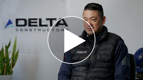 Photo of man wearing black Delta Constructors puffer vest looking at camera with play icon overlayed