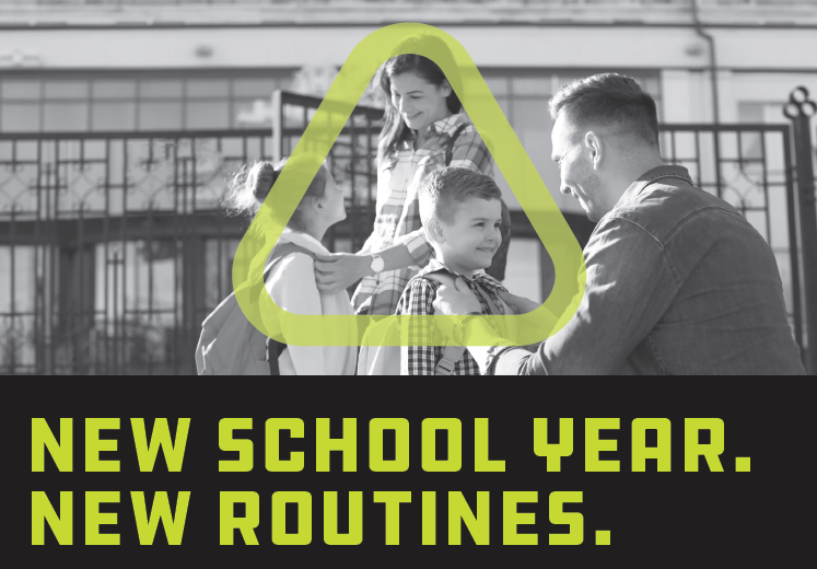 A mother situates her child's backpack straps while a father crouches on the ground doing the same thing for their other child. 