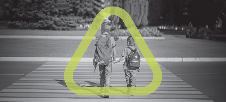 Black and white photo of two children walk across a crosswalk wearing backpacks set inside the Get Home Safe triangle.