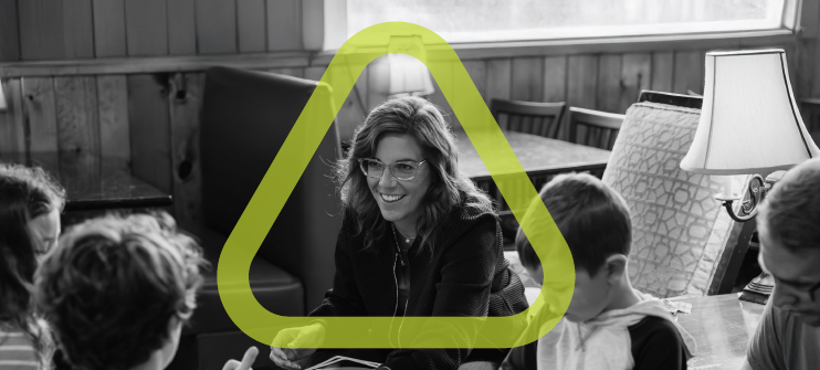 Woman sitting down smiling at children surrounding a low table playing a game. 