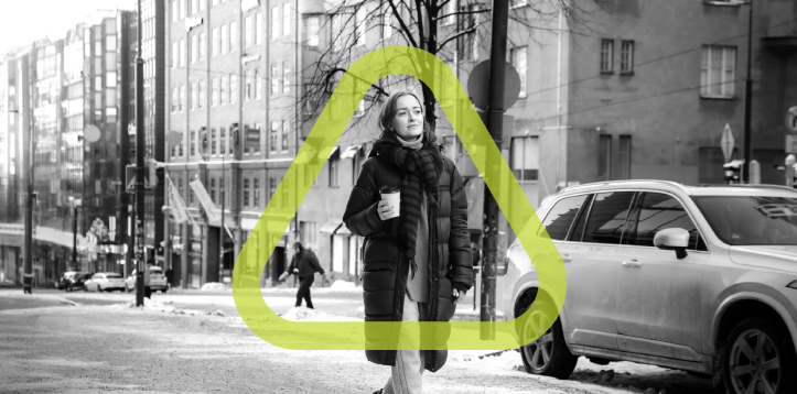 Black and white photo of woman walking on snowy sidewalk in a city with the green GHS triangle surrounding her.