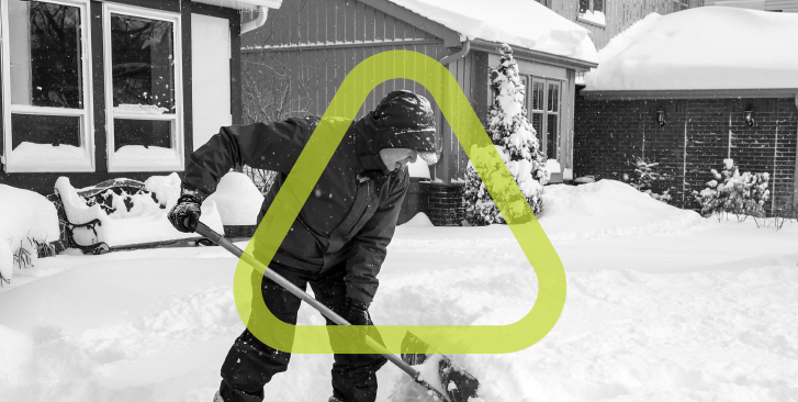 Black and white photo of man shoveling snow with the safety green Get Home Safe triangle surrounding him