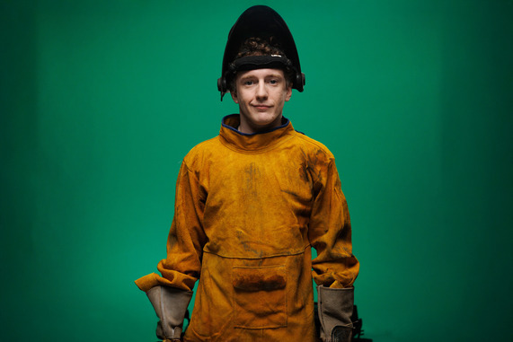 Man wearing welding gear and mask against a green background