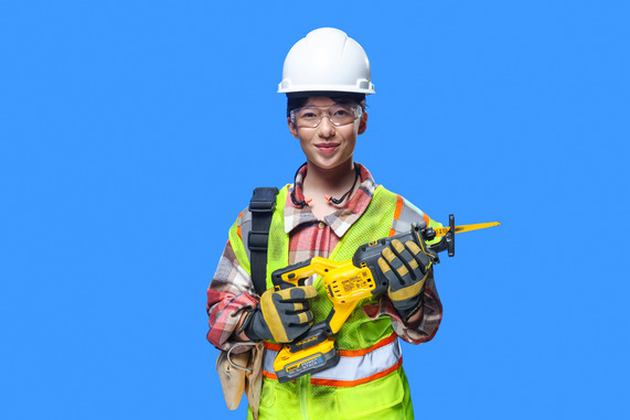 Female worker wearing a safety vest, hard hat, safety glasses, and gloves holds a battery-powered saw.