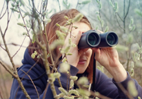 Woman peering through branches with binoculars