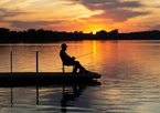 Man fishing from a dock at sunset