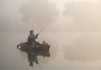 Man fishing from a kayak on a foggy day