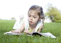 Girl laying in grass reading something