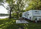 An RV camped under the trees with people sitting outside on chairs