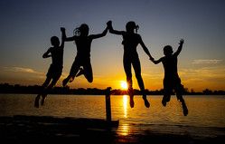 Silhouettes of children jumping into a lake at sunset