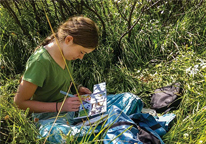 Girl sitting in grass working on a nature journal