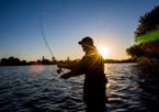 Silhouette of man fly fishing at sunset