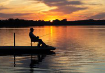 Man fishing from a dock at sunset