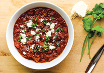 Bowl of venison chili next to some cilantro 