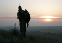 Silhouette of hunter carrying harvested turkey at sunset