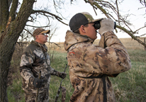 Two young hunters using binoculars while hunting turkey