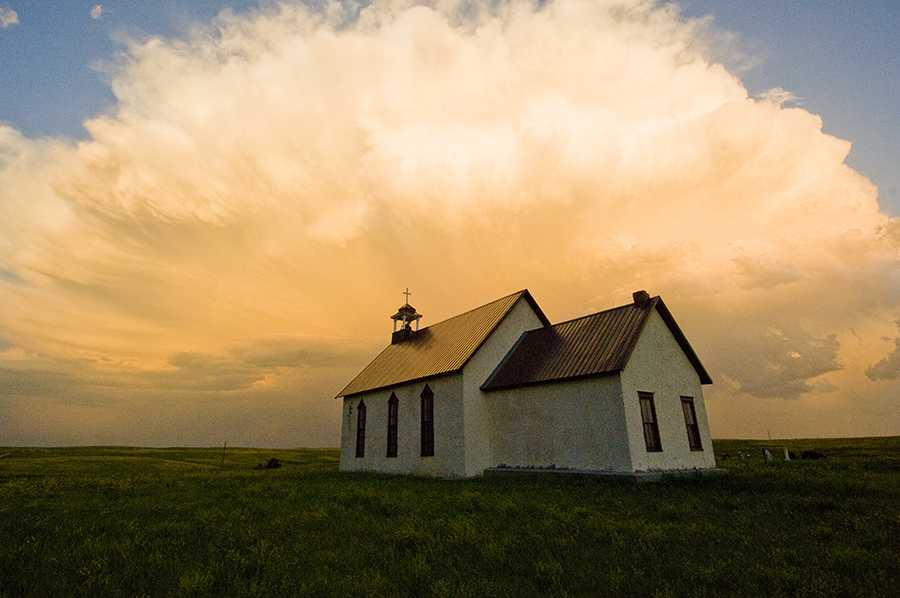 Abandoned church on grasslands with impressive orange cloud formation behind it.