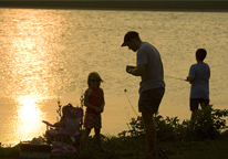 Silhouette of family fishing by bank at sunset