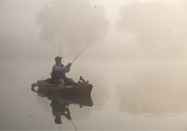 Angler kayak fishing in misty lake