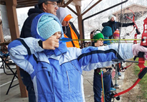 Kid in winter coat practicing archery at Archery on Fire event