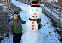 Boy standing by snowman he made