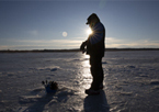 Silhouette of angler fishing through the ice