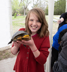 Girl smiling and holding a turtle during the school day at the Fort Kearny Expo