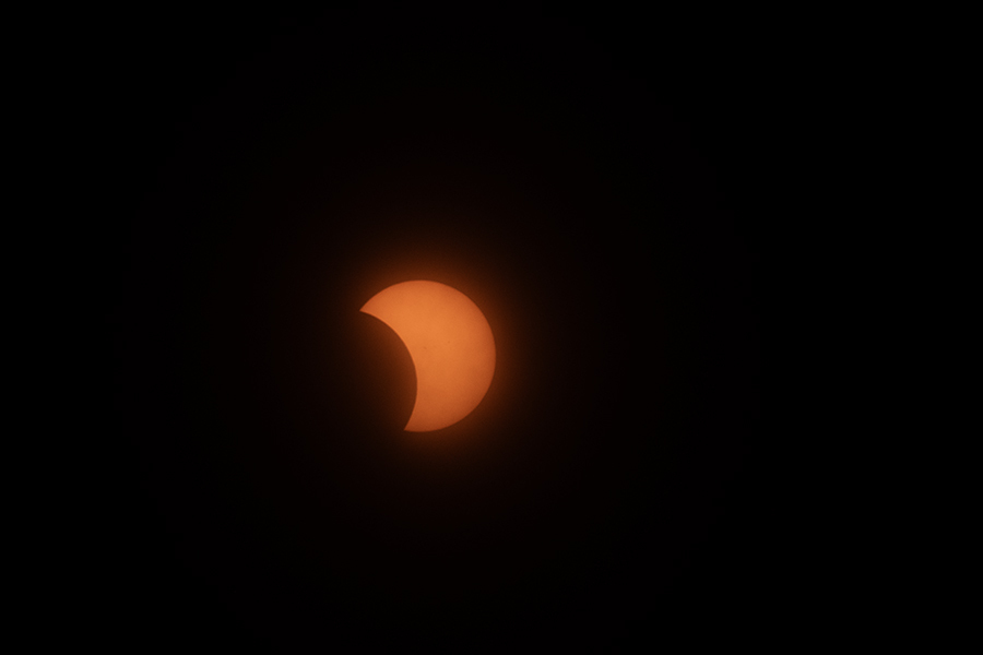 Dark sky with partial eclipse, showing an orange sun with a crescent missing.