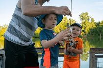 Father helping young kids to fish off a dock