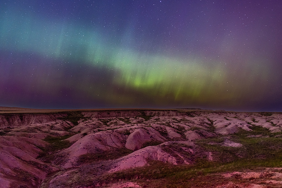 Green northern lights glow over a rocky butte landscape in the Oglala National Grasslands