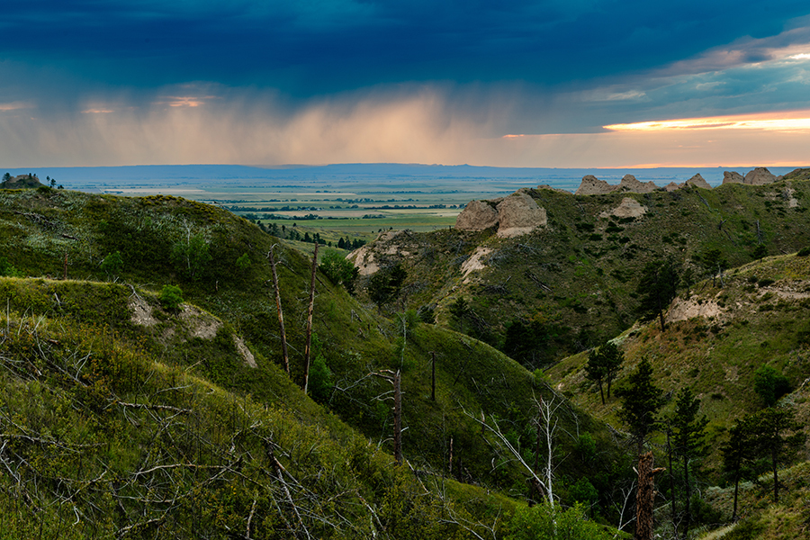 Light rain falls in the distance, beyond the landforms and canyons of the Nebraska National Forest and White Valley.