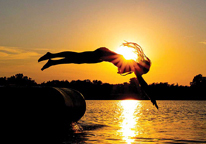 Silhouette of a girl diving into a lake at sunset, with sun rays shooting over her shoulder