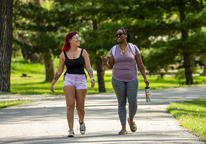 Two young women walking on a paved trail with trees in background