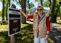 Eleanor Shimek stands by her camper with her hand on the "campground host" sign