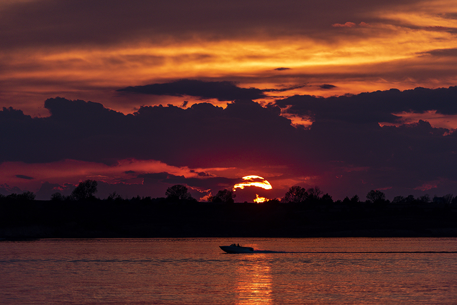 A boat cruises along Sherman Reservoir beneath a brilliant red and orange sunset.