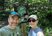 Couple posing by Your Parks Adventure selfie sign along wooded trail