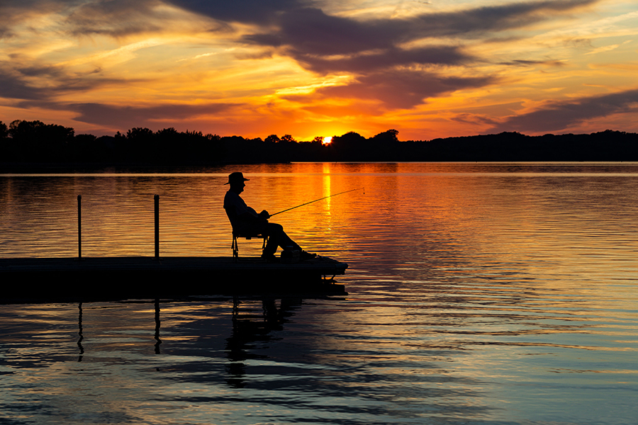 Silhouette of an angler fishing from a boat dock under a brilliant orange sunset.